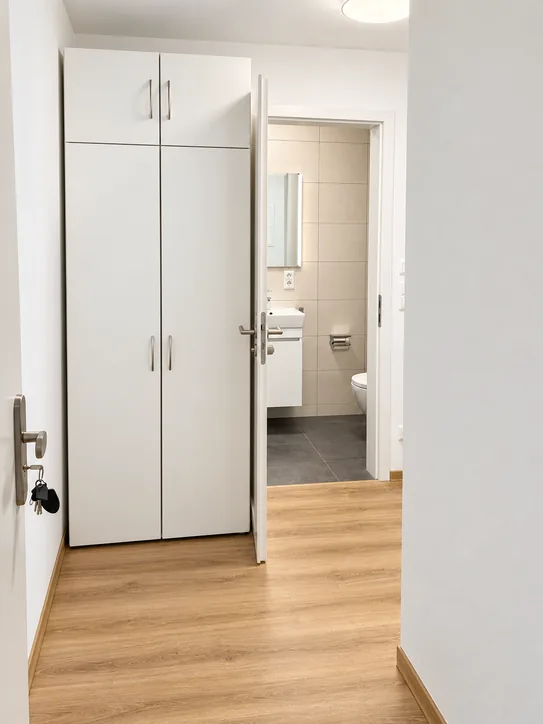 Flur im Apartment mit weißem Einbauschrank, Vinylboden in Holzoptik und Blick ins Duschbad