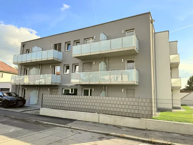 Das fertige Haus von der Straße: graue Fassade, Balkonbänder mit Glasbrüstung, Einfriedung zum Gehweg