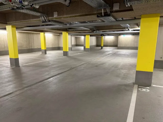 Tiefgarage mit markierten Stellplätzen, gelb gestrichenen Stützen und Beleuchtung